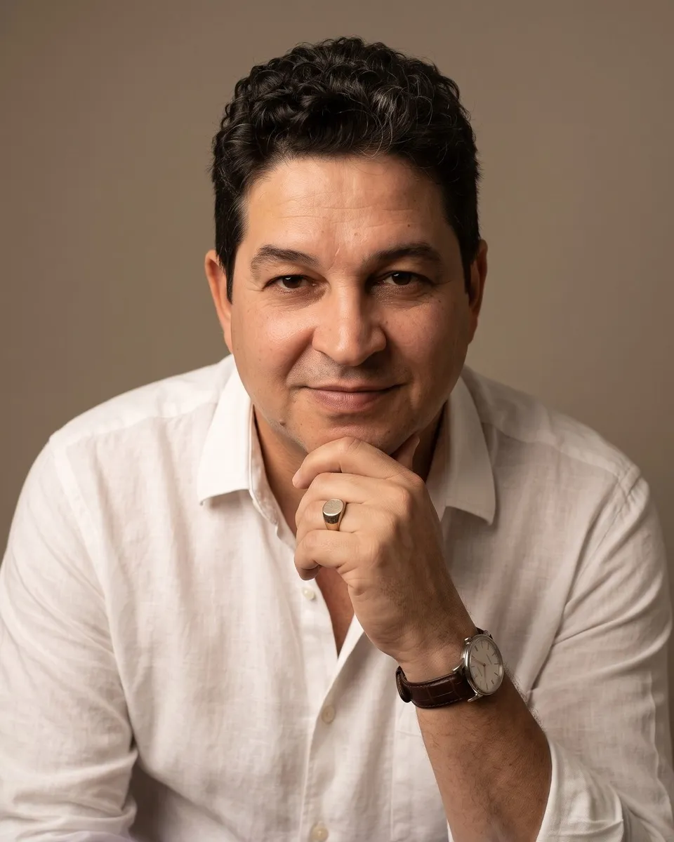 Dr. Carlos Fabiano de Oliveira, de camisa branca, sorrindo com a mão apoiada no queixo